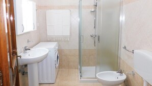 Un baño con ducha envuelta en vidrio, dos lavamanos, inodoro y espejo.