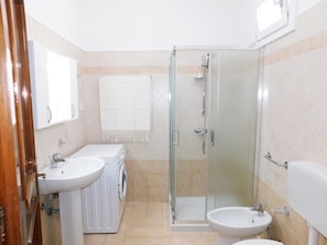 A bathroom with a glass-enclosed shower, two sinks, a toilet, and a mirror.