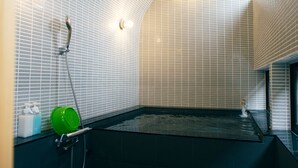 Un baño moderno con una bañera negra, zona de ducha y dispensador de jabón verde.