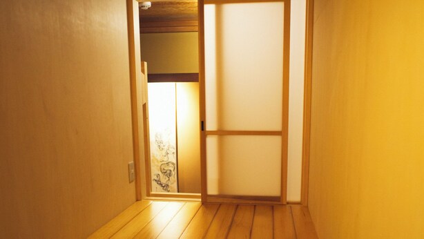 Un pasillo estrecho con suelo de madera y un felpudo de tatami en la entrada.