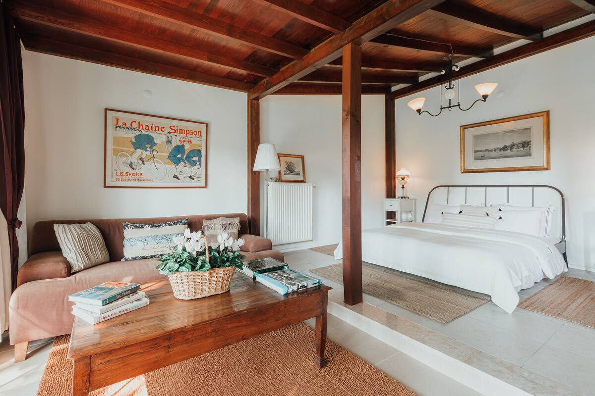 A bedroom with a white bed, a wooden ceiling, a nightstand, and a framed picture on the wall.