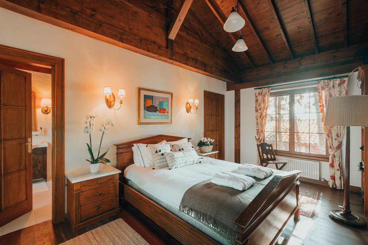 A bedroom with a wooden bed, bedside tables, a nightstand, a window with curtains, and a floor lamp.