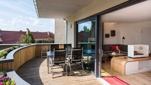 Ein modernes Wohnzimmer mit einer gebogenen Holzbank, einer Glastür, die auf einen Balkon führt, und einem kleinen weißen Schrank.