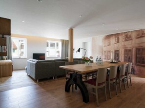 A modern living room with a wooden dining table, grey sofa, and a large window.