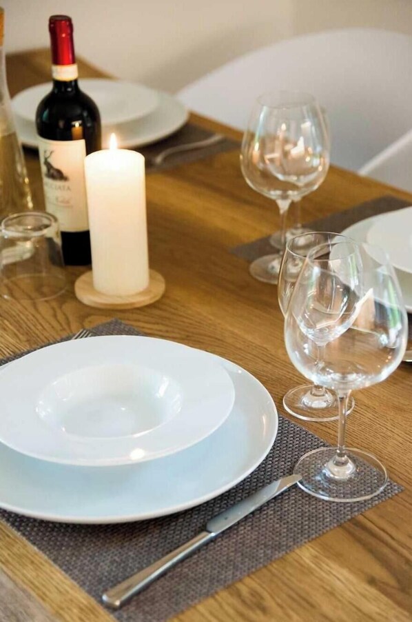 Une table à manger dressée avec une assiette blanche, un verre à vin, une bougie et une bouteille de vin.