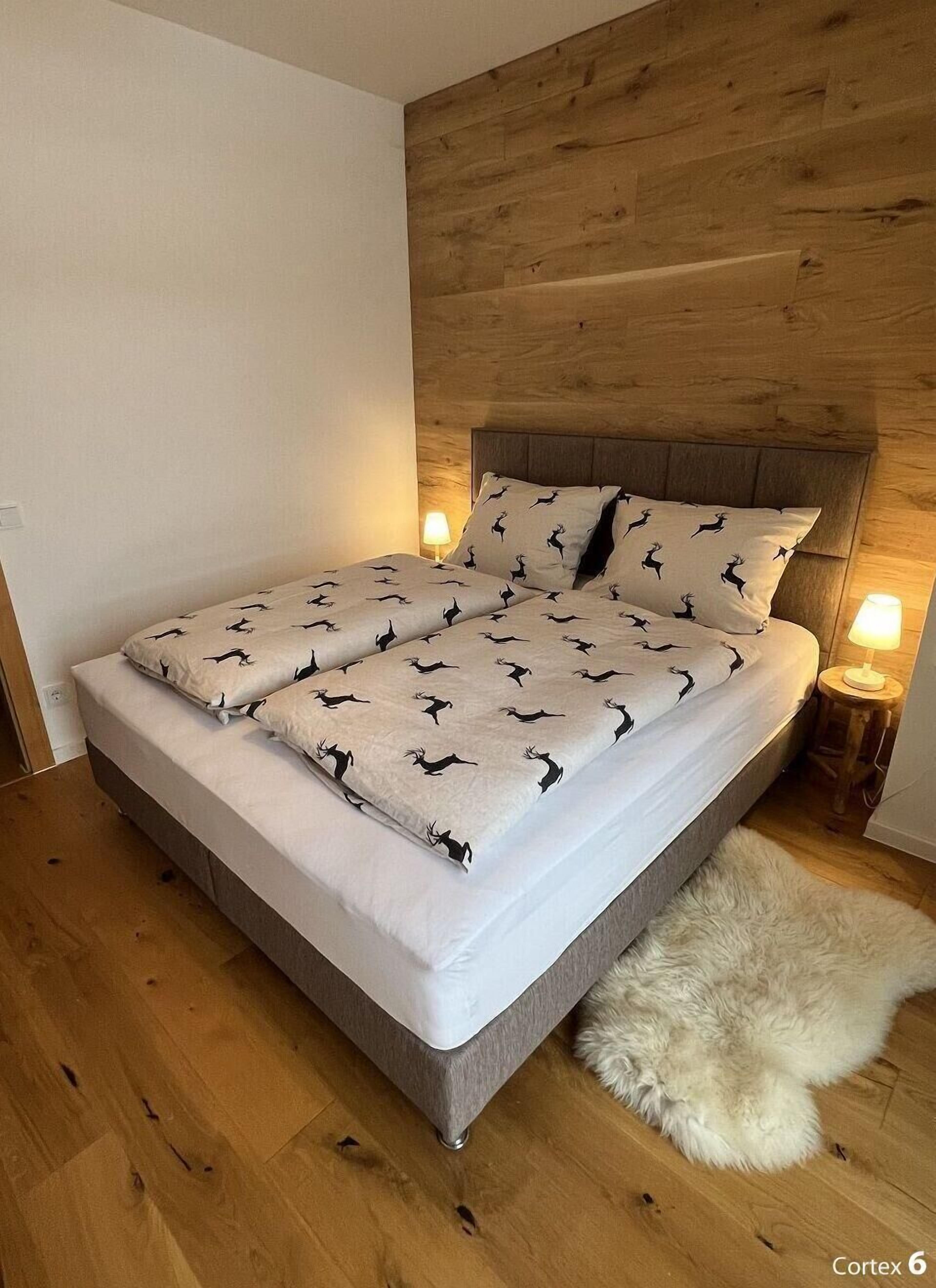 A bedroom with a wooden headboard, a bed with patterned bedding, a fluffy rug, and bedside lamps.