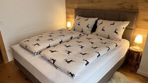 Un dormitorio con cabecera de madera, cama con ropa de cama estampada, una alfombra mullida y lámparas de noche.