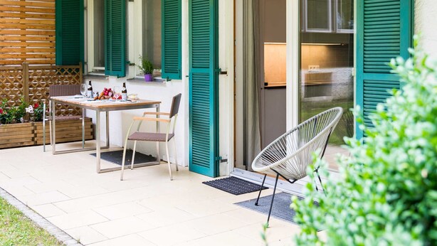 Un patio exterior con una mesa y sillas, una silla de mimbre y una cerca de madera.