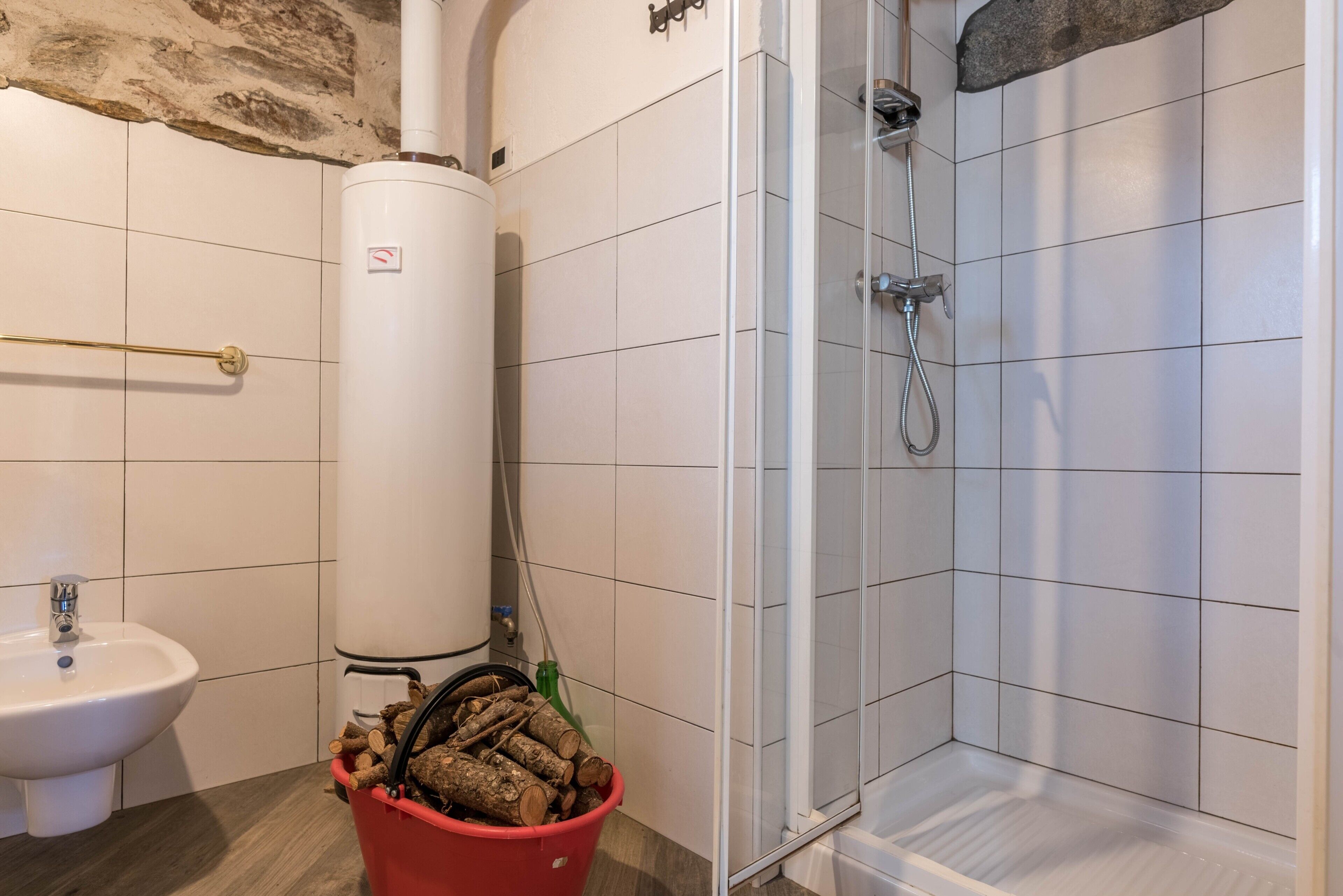 A bathroom with a white sink, a red bucket of logs, a white toilet, and a shower area with white tiles.