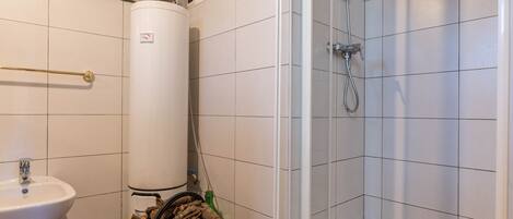 A bathroom with a white sink, a red bucket of logs, a white toilet, and a shower area with white tiles.