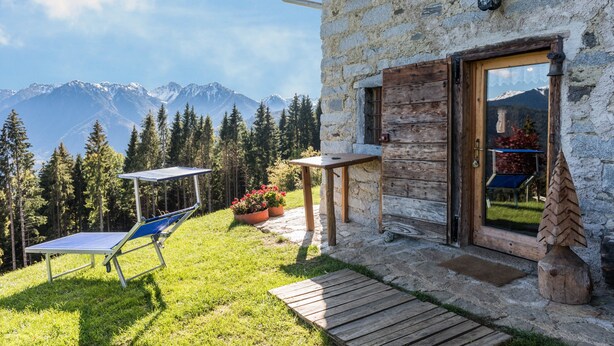 A stone building with a wooden door, a small table, and a chair outside. - Holiday Home “Baita dai Cotai” in Fantastic Scenery with Mountain View (Porte di Rendena)
