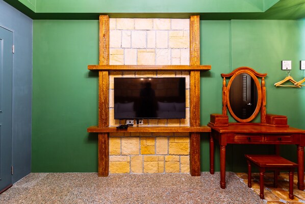 Quarto com lareira de pedra, televisão, escrivaninha de madeira e espelho.