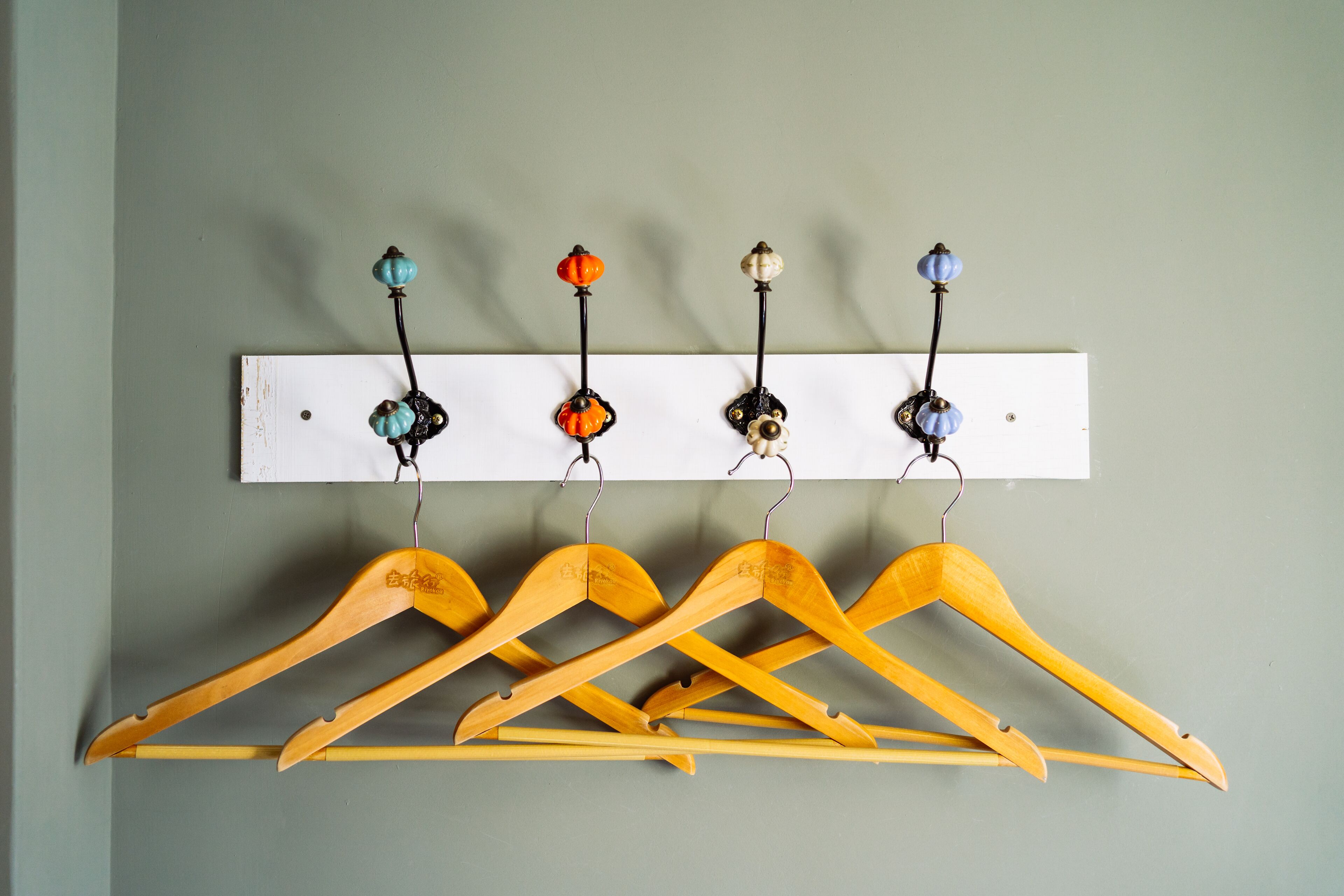 A wooden coat rack with multiple hangers and a white wall-mounted hook with decorative elements.