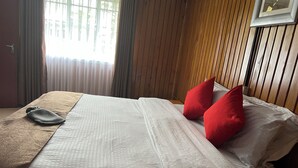 Un letto rifatto con lenzuola bianche e due cuscini rossi, una coperta marrone e una testiera in legno.