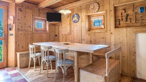 Een houten interieur met een eettafel, stoelen, een klok en een tv aan de muur.