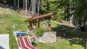 Een terras met een houten pergola, een gestreept lounge stoel, een stenen tafel en een kleine tuin.
