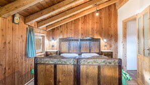 Een kamer met houten lambrisering, een bed, twee nachtkastjes, een klok en een raam.
