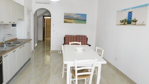 Una cocina con armarios blancos, un lavamanos doble y una zona de comedor con una mesa y sillas blancas.