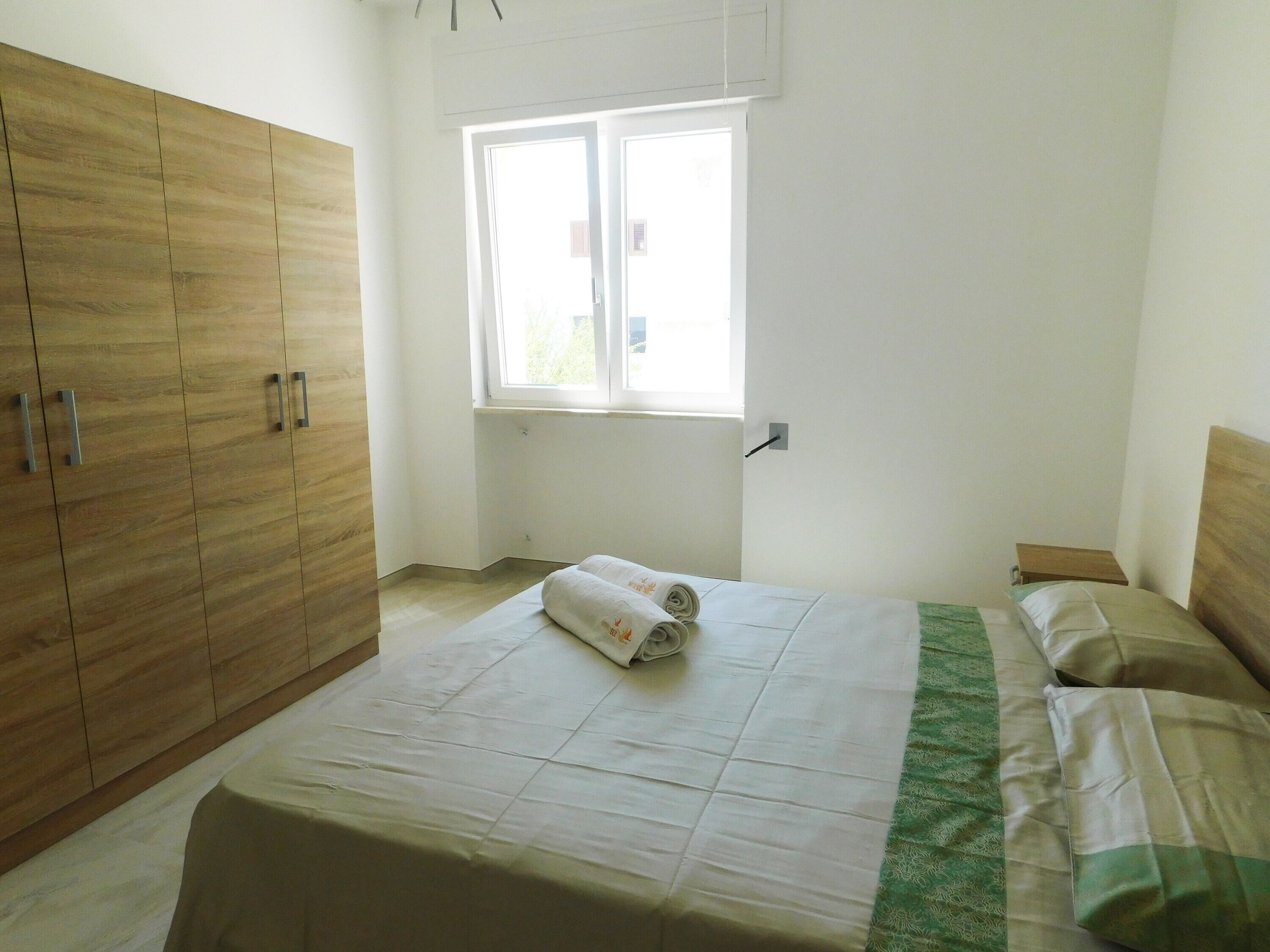 A bedroom with a bed, a window, and wooden wardrobe.