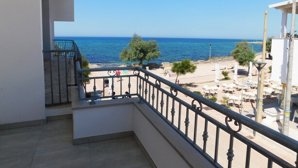 Un balcón con vista al mar, mobiliario exterior y cielo despejado.