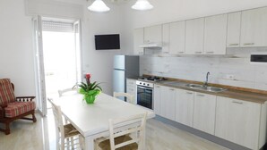 Una cocina con armarios blancos, una estufa y un lavamanos. Hay una mesa de comedor con sillas y una planta en maceta.