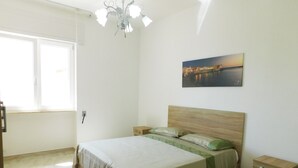 Un dormitorio con cama, mesitas de noche, una ventana y un cuadro colgado en la pared.