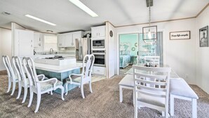 Une cuisine compacte avec des meubles blancs, un îlot central et un coin repas avec des chaises blanches.