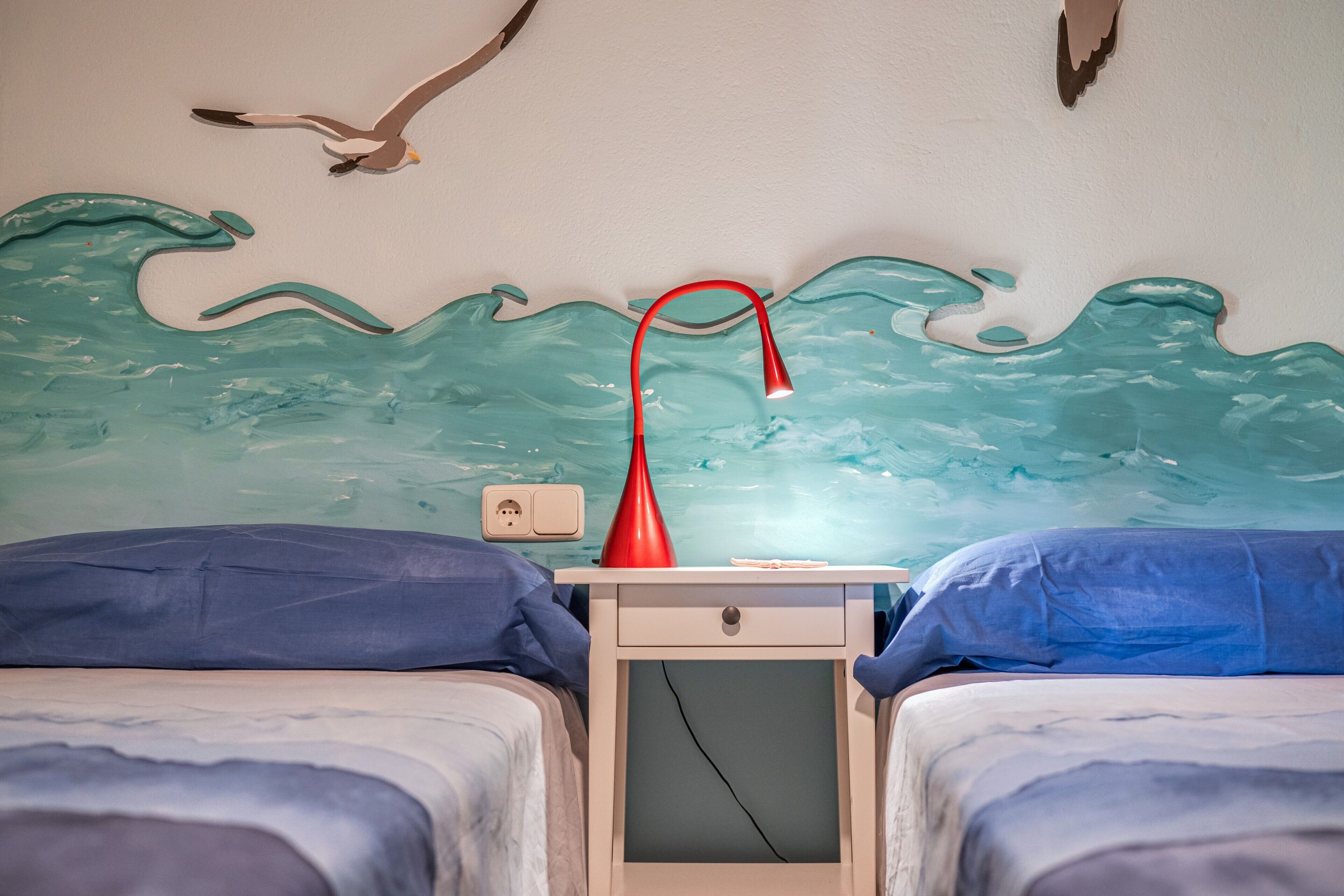 Une chambre avec deux lits, une table de chevet avec une lampe et une fresque murale.
