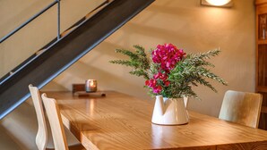Une table à manger en bois sur laquelle est posé un vase blanc contenant des fleurs roses et des feuilles vertes.