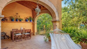 Une terrasse extérieure avec une table et des chaises en bois, un hamac et des plantes en pot, le tout installé sous une structure en arc de cercle.
