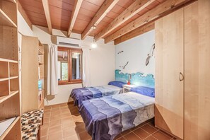 Une chambre avec deux lits, des poutres en bois, une fenêtre avec des rideaux, une fresque murale et une table de chevet avec une lampe.