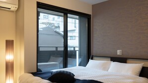 Una habitación de hotel con un ventanal grande, una cama con ropa blanca y un papel tapiz estampado.