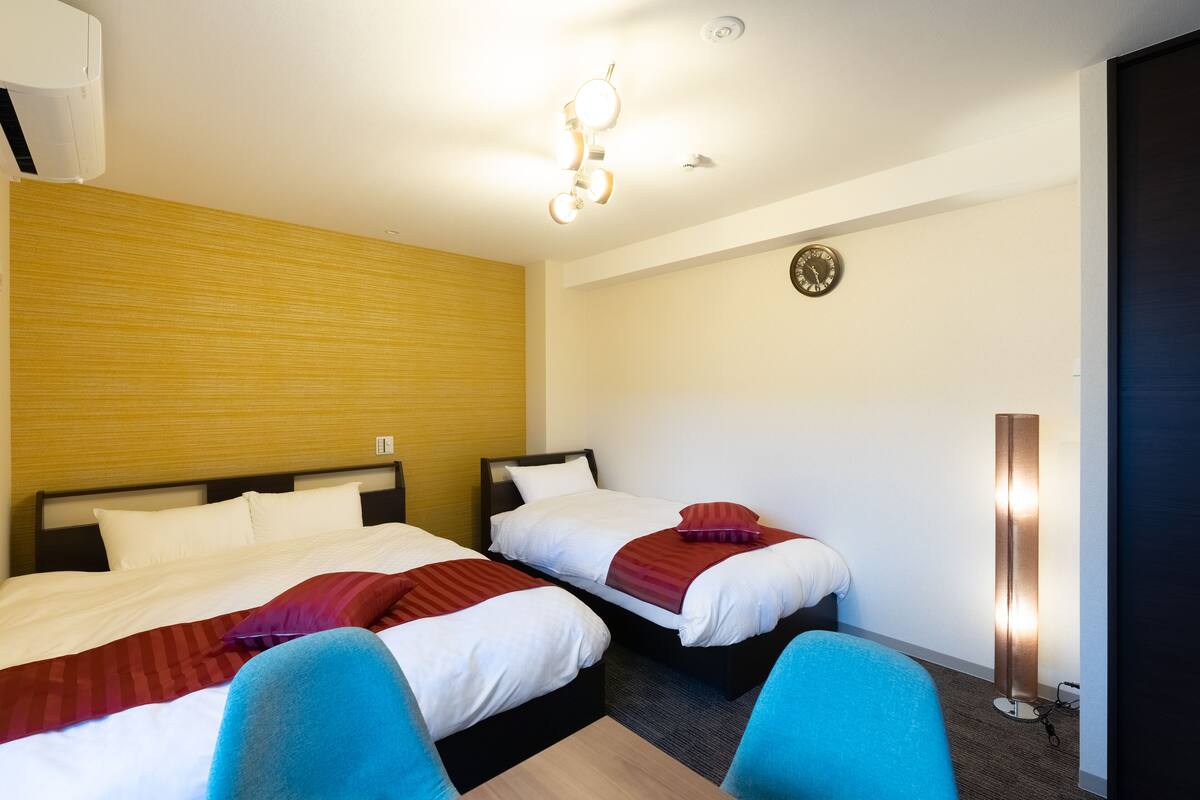 A hotel room with two beds, a wooden accent wall, a clock, and a standing floor lamp.