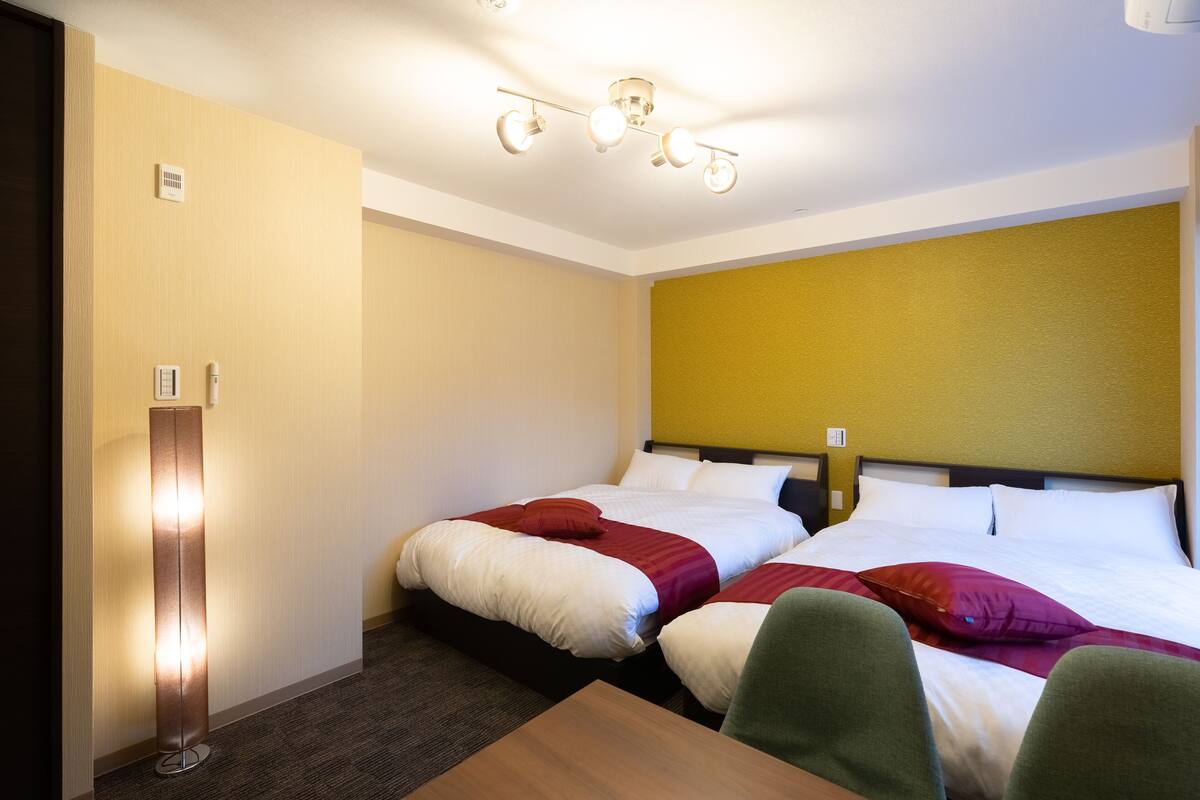 A hotel room with two beds, a desk, and a standing lamp.