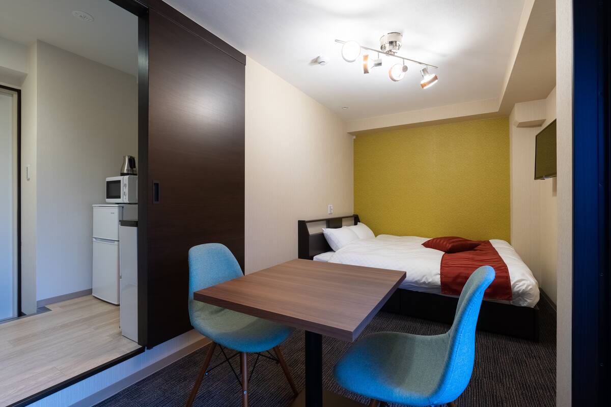 A hotel room with a bed, a desk, two chairs, a microwave, and a small kitchenette.
