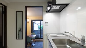 Una cocina moderna con electrodomésticos de acero inoxidable, un comedor con mesa y sillas, y vistas a un balcón desde una puerta abierta.
