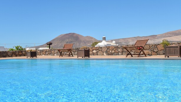 A swimming pool with lounge chairs and a stone wall, with a mountain and white building in the background. - Beautiful Villa La Petit with Pool, Terrace, Garden and Wi-Fi (GUATIZA)