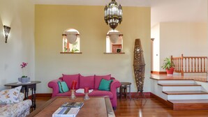 A living room with a pink sofa, a coffee table with magazines, a chandelier, and a staircase. - Beautiful Villa La Petit with Pool, Terrace, Garden and Wi-Fi (GUATIZA)