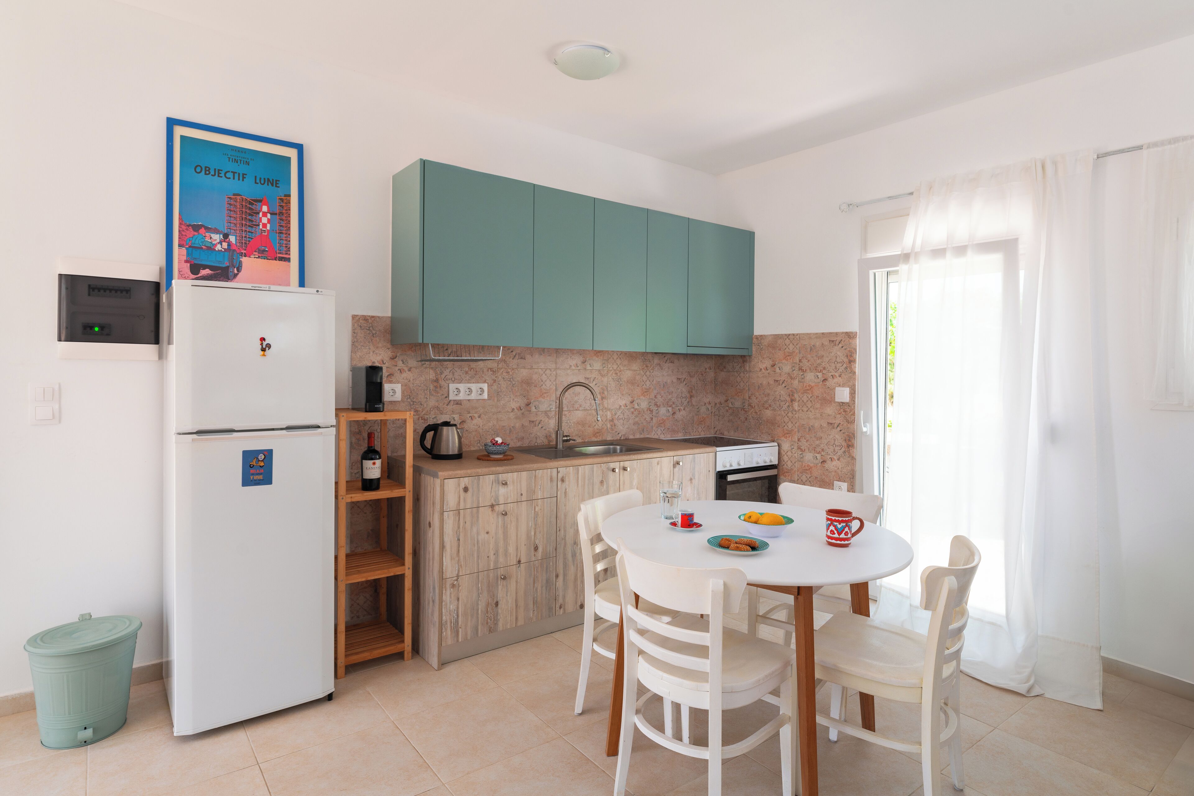 Una cocina compacta con gabinetes azul verdoso, un refrigerador blanco y una mesa de comedor con sillas.