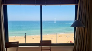 A room with a large window overlooking a beach, a chair, and a lamp. - Albufeira Beach Cliffs House by Rentals in Algarve (Albufeira)