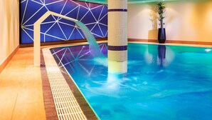 An indoor swimming pool with a geometric wall design, a central column, and a water feature.