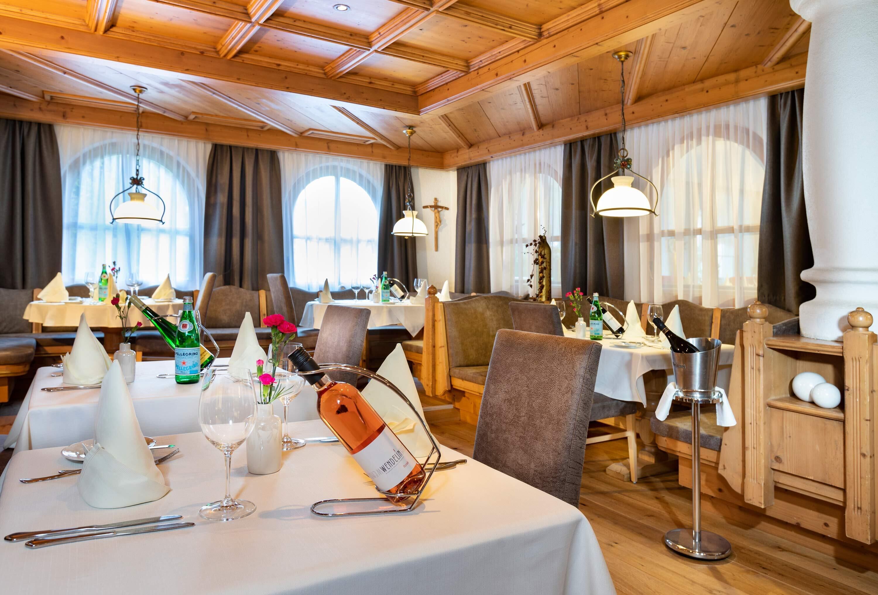 Un comedor con vigas de madera, mesas dispuestas con manteles blancos, copas de vino y una botella de vino.
