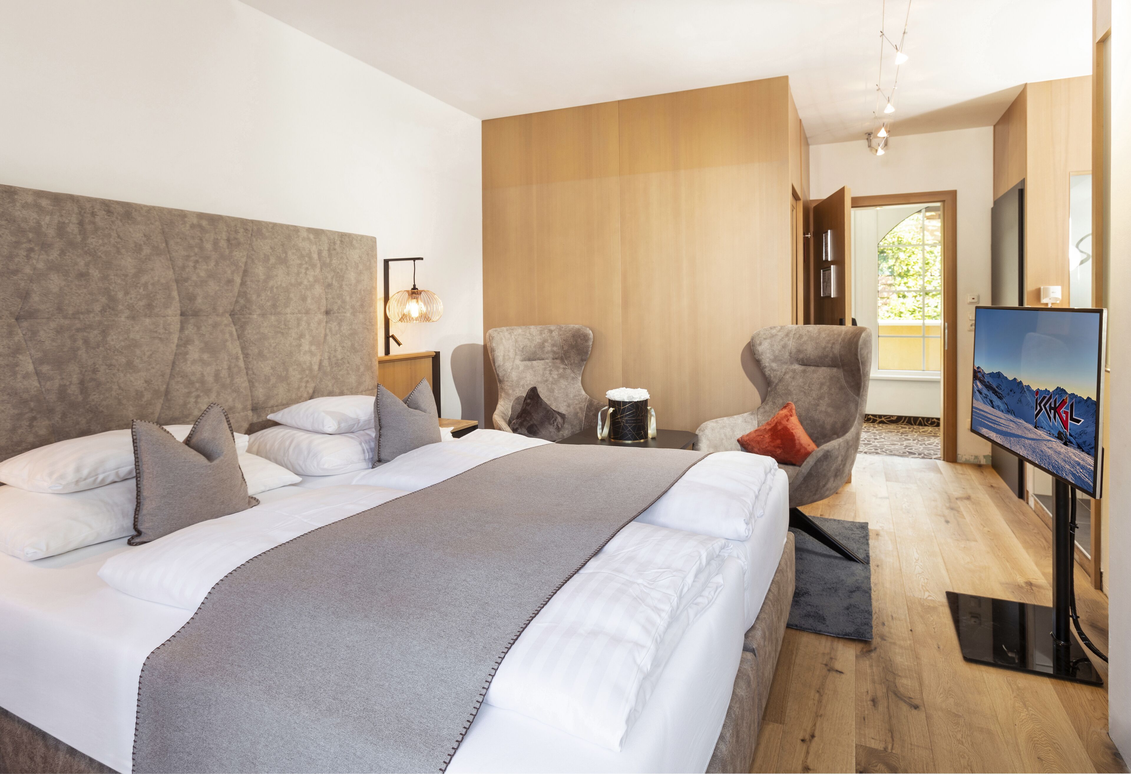 A modern hotel room with a large bed, a TV, a coffee table, and a seating area with chairs.