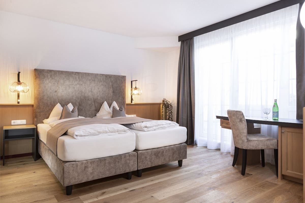 Quarto de hotel moderno com uma cama grande, luminárias de cabeceira, uma escrivaninha e uma cadeira.