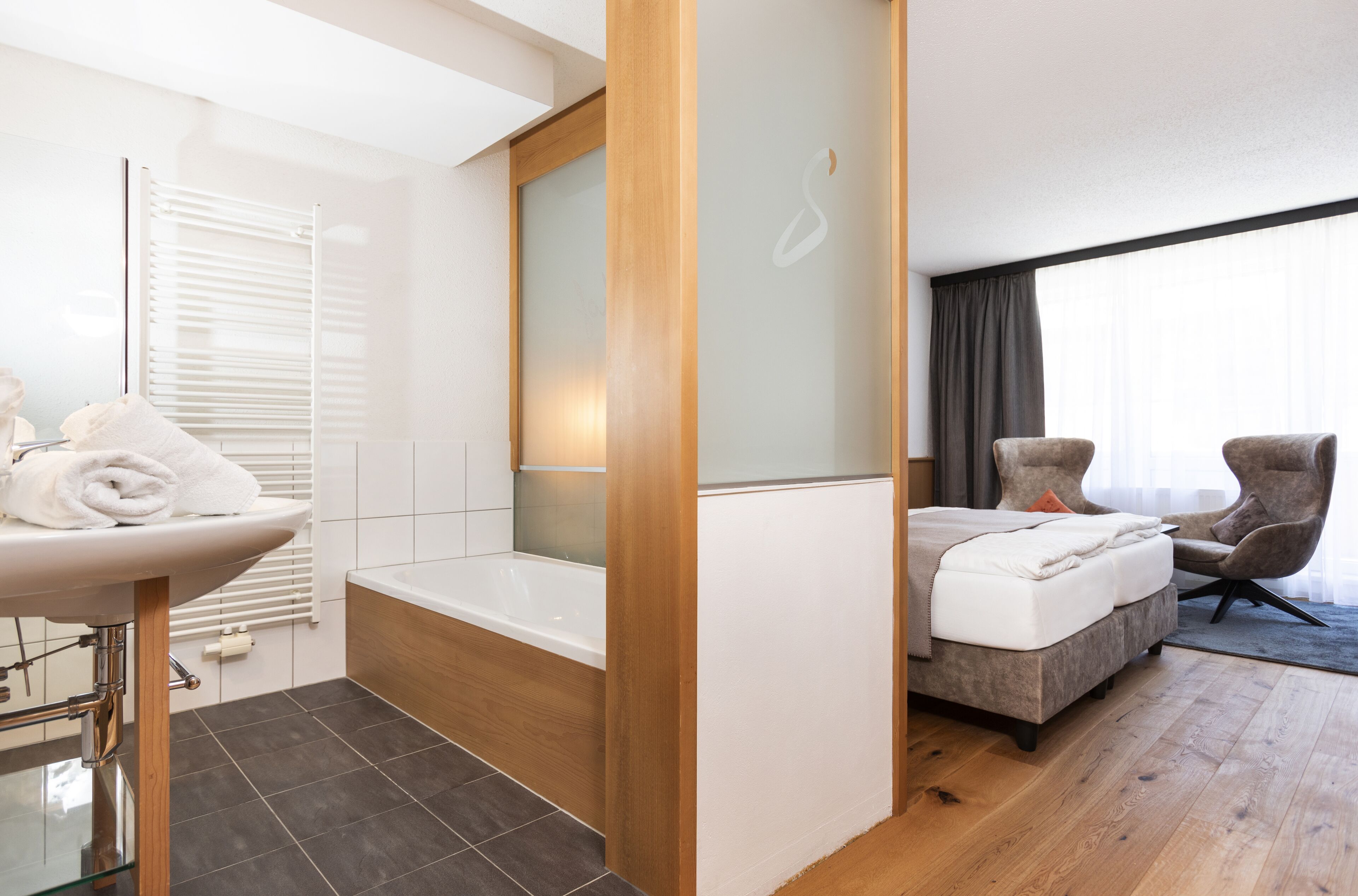 Moderni hotellihuone, jossa on kylpyhuone, sänky ja oleskelualue.