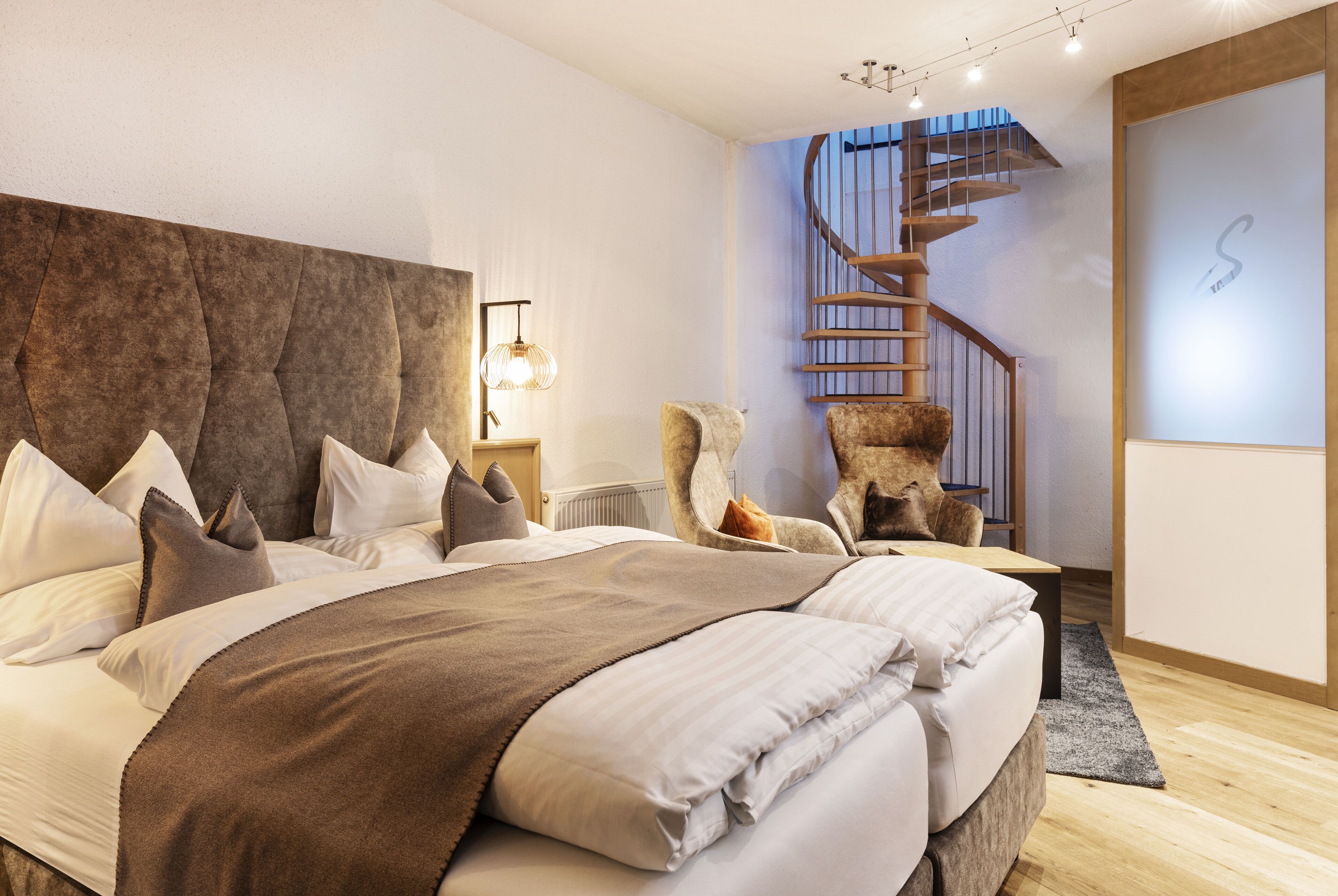 A modern bedroom with a large bed, a wooden headboard, a spiral staircase, and a minimalist decor.