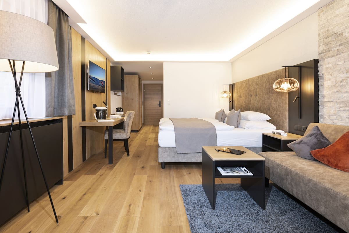 Quarto de hotel moderno com cama, sofá, escrivaninha e televisão.