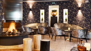 A modern lounge area with a central fire feature, seating, and ambient lighting.