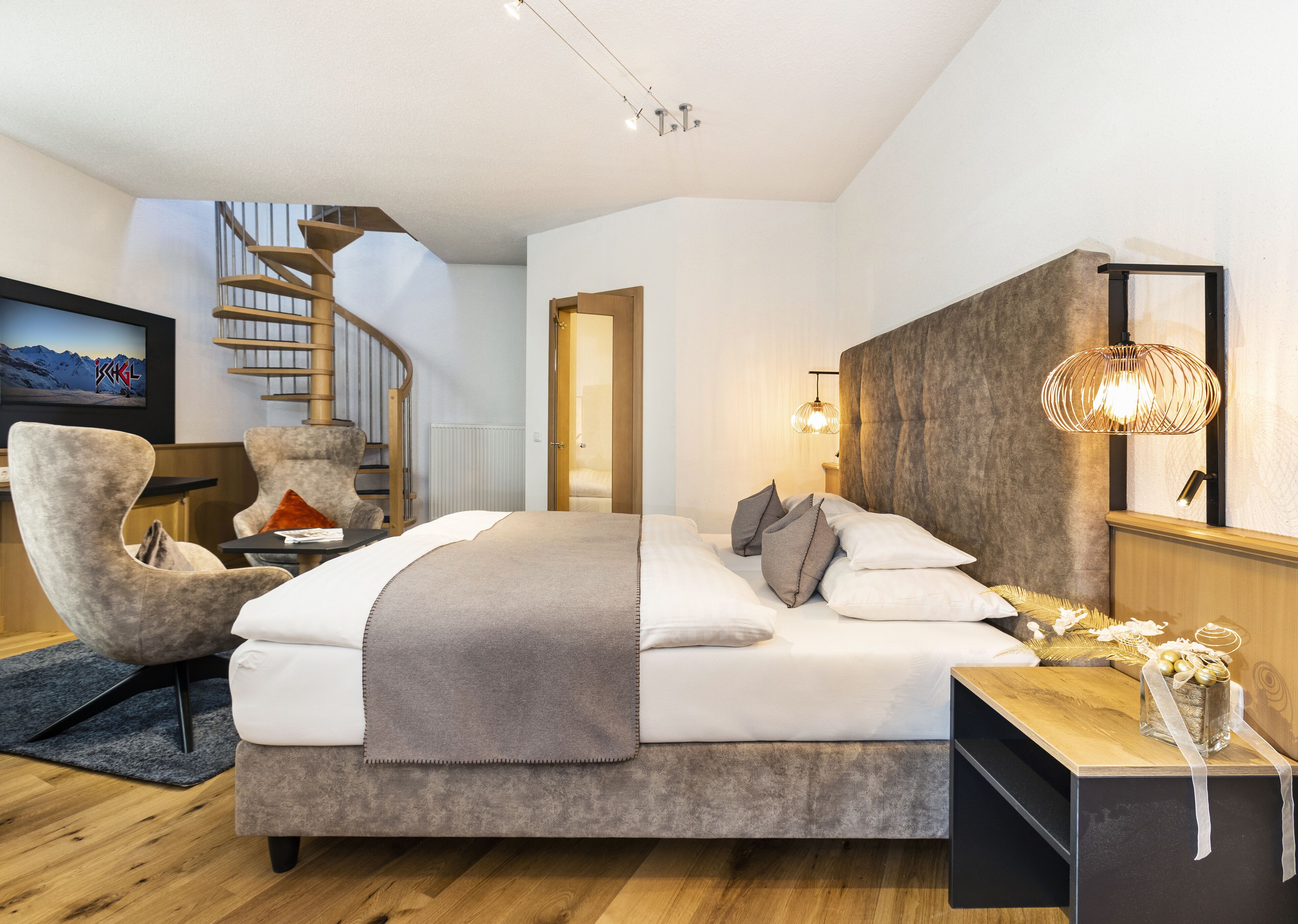 A modern bedroom with a large bed, a chair, a wooden nightstand, a TV, and a spiral staircase.