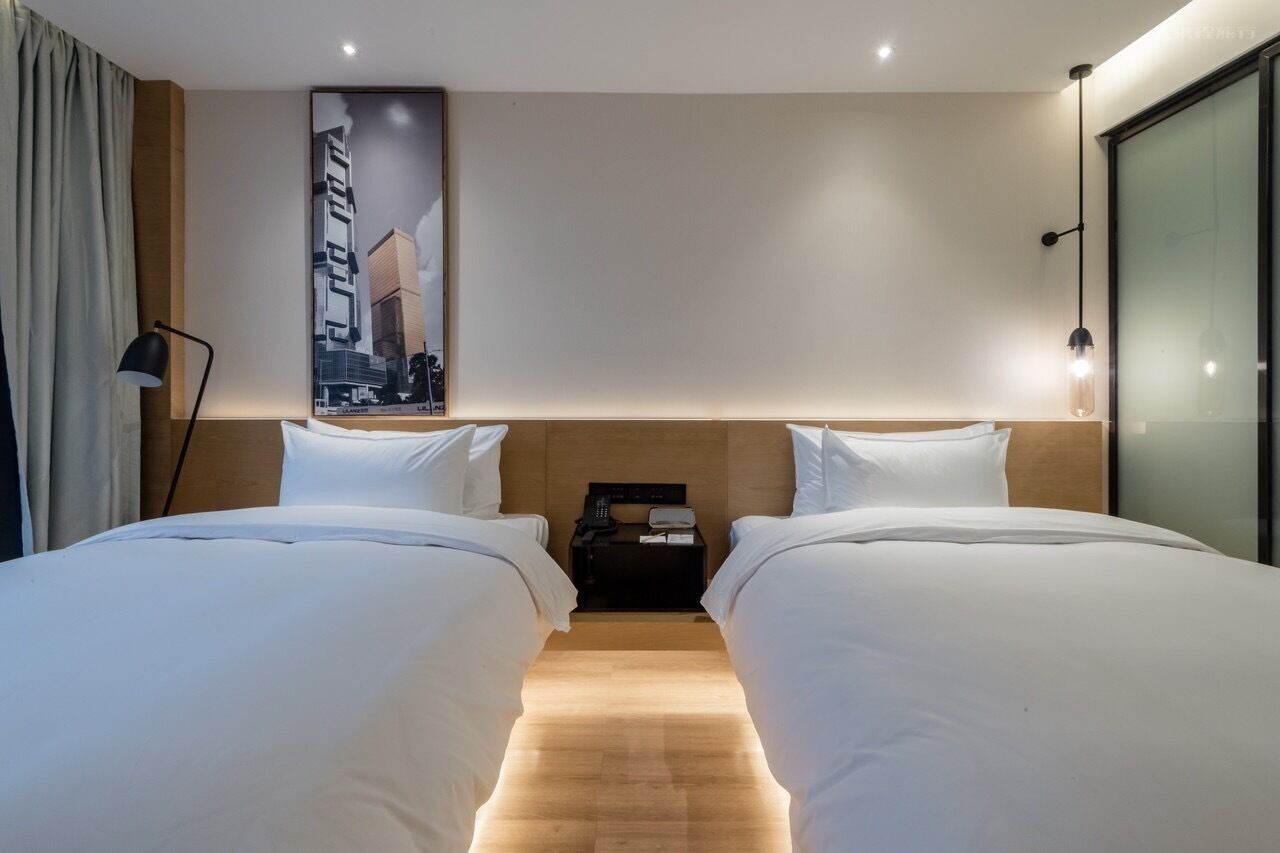 A hotel room with two beds, a nightstand, a lamp, and a poster on the wall.